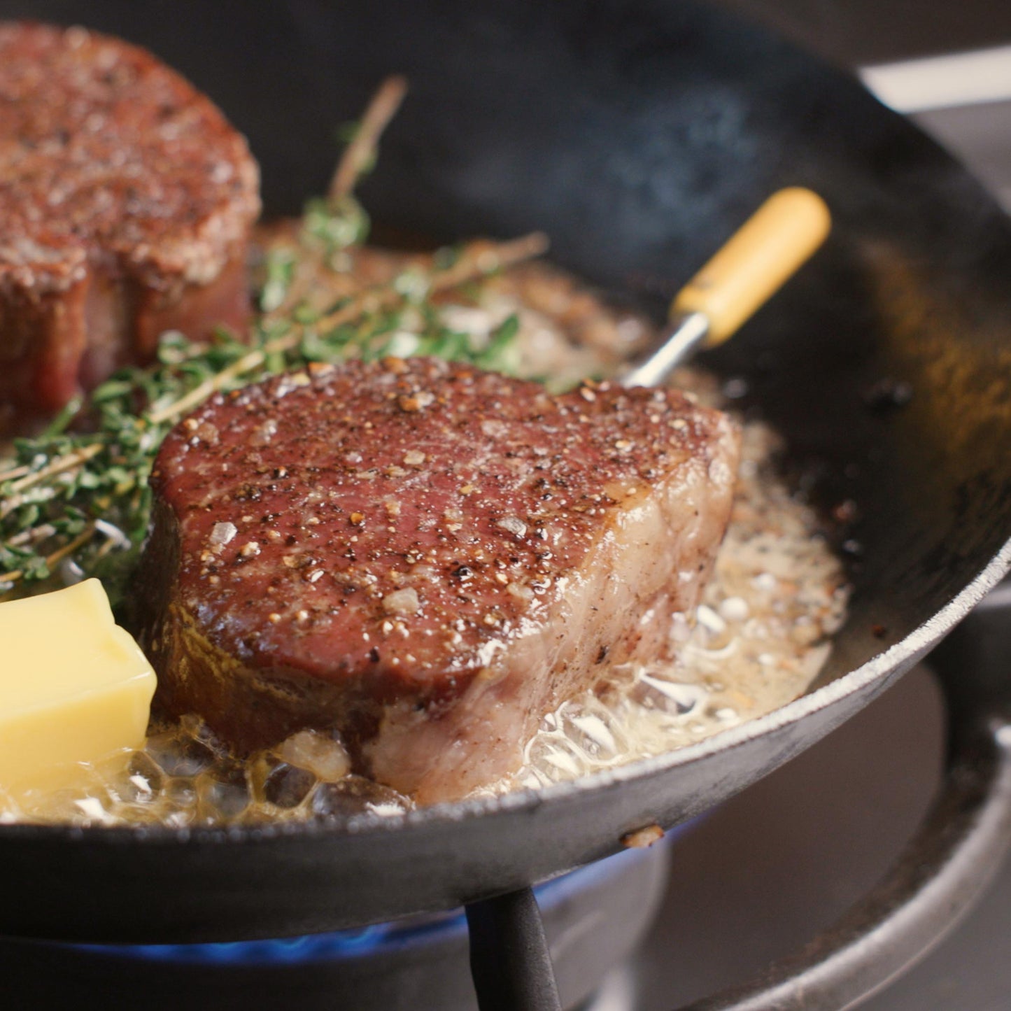 Steak (filet) in a pan with Predictive Thermometer inserted, butter and herbs. 